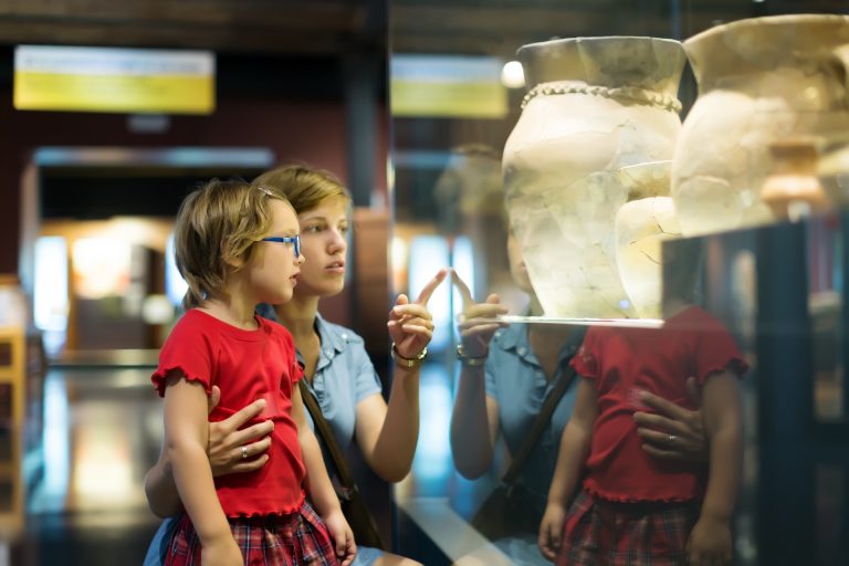 Mor og barn ser på gamle leirkrukker i en montre på et museum